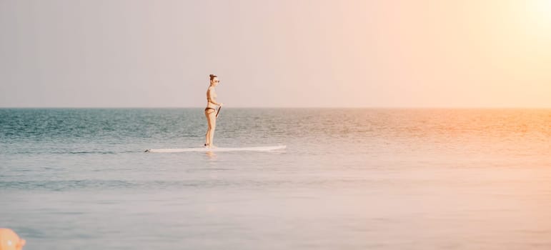 Sea woman sup. Silhouette of happy middle aged woman in rainbow bikini, surfing on SUP board, confident paddling through water surface. Idyllic sunset. Active lifestyle at sea or river