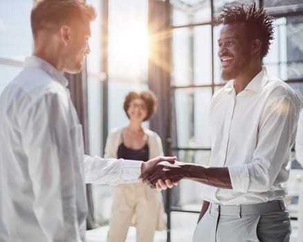 Glad to work with you. Young modern men in smart casual wear shaking hands and smiling while working in the creative office