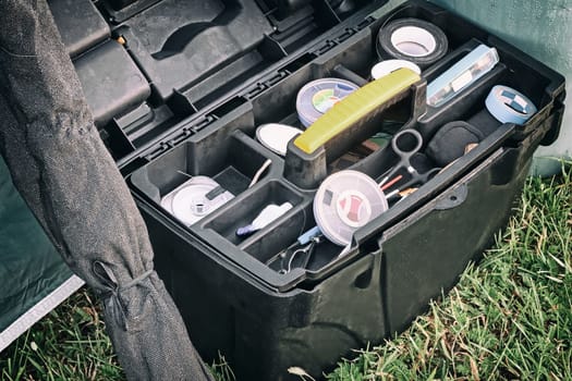 On the grass in a container are various items needed for fishing.