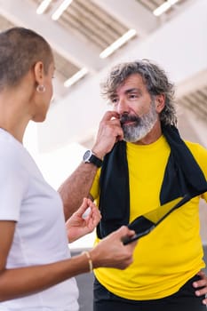 senior sports man watching progress of his workout on a tablet and discussing the results with his personal trainer, concept of healthy and active lifestyle