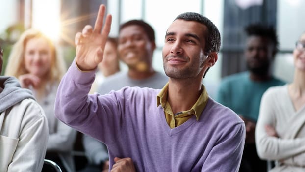 Group of young people sitting on conference together while one man raising his hand