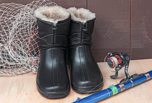 On the table located items for fishing: landing net, spinning and warm waterproof boots.