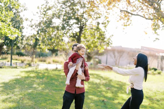 Laughing mom pulls her hands to a little girl sitting in dad arms. High quality photo