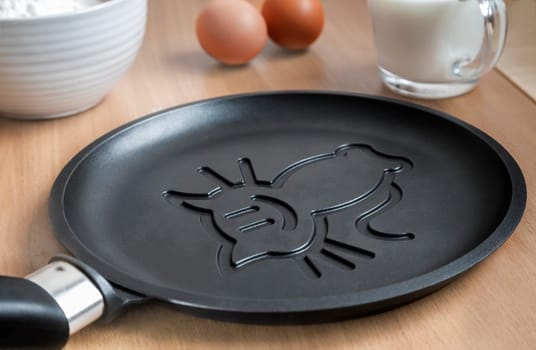 A cast-iron skillet with ceramic coating for cooking pancakes. Next to the ingredients for pancakes: flour, eggs, milk.