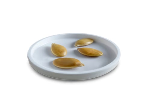 On a white saucer large pumpkin seeds. Presented on a white background.
