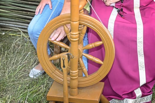 The woman in the national dress shows an old wooden spinning wheel.