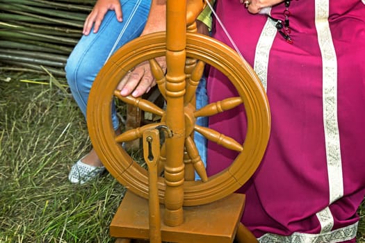 The woman in the national dress shows an old wooden spinning wheel.