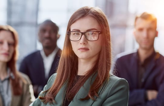 Young executive smiling and standing in a bright room with her team behind her