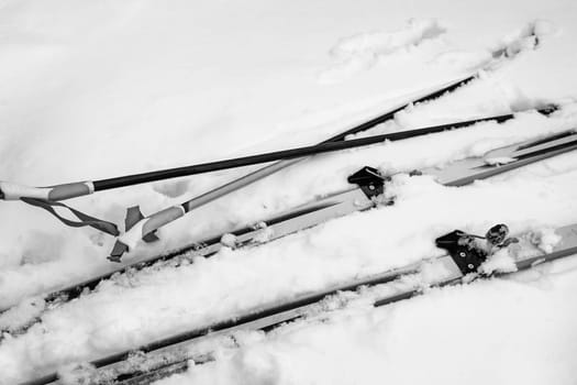 Ski poles and skis with bindings lay in the snow. The view from the top.
