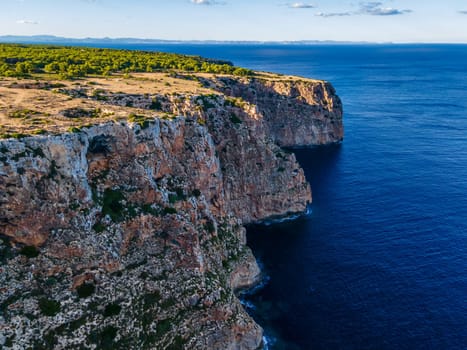 Rocky cliffs plunge into the deep blue sea on a summer day.