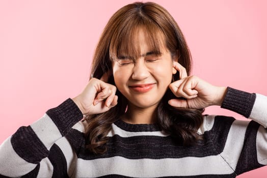 Asian beautiful young woman closed ears with fingers and close eyes, studio shot isolated on pink background, portrait female covers ears from music loud noise with copy space, Deaf concept