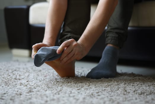 Man at home in morning puts gray socks on his leg. For a long time do not change clothes concept