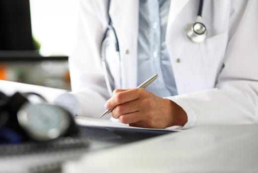 Hands of female GP making notes with silver pen while receiving visitor close-up