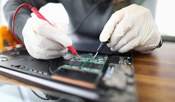 Male hands in white protective glove hold contact probe an electronic circuit tester. Laptop repair and technology concept