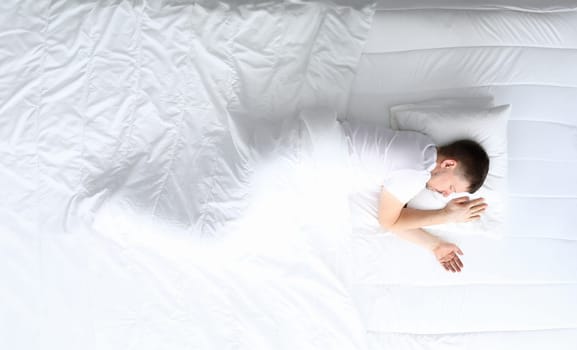 Young caucasian handsome man sleeping on white bed home portrait. Top view background