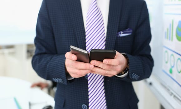 Close-up of manager using modern gadgets and wearing trendy suit with striped tie and classy shirt. Man posing in modern office. Company meeting concept