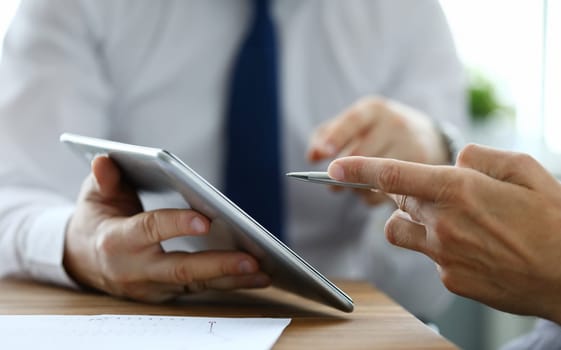 Two businessman are looking and studying statistics on tablet display closeup. Male hand opponent holds pen and points out problem collaboration business coach partnership digital sign concept