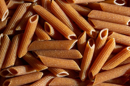 Uncooked Whole Grain Penne Rigate Pasta: A Culinary Canvas of Whole Wheat Macaroni, Creating a Lively and Textured Background for Gourmet Cooking. Whole Grain Dry Pasta. Whole Wheat Raw Macaroni