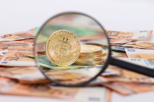 A Stack of Bitcoin Coins Visible Through a Magnifying Glass on the 50-Euro Banknotes. Euro Currency and Crypto Currency. Orange Paper Money. A Lot of Fifty-Euro Bills. Anonymous Payments Concept