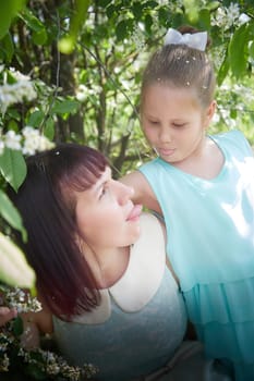 Happy mother and daughter enjoying rest, playing and fun on nature on a green lawn and with blooming apple tree in the background. Woman and girl resting outdoors in summer and spring day