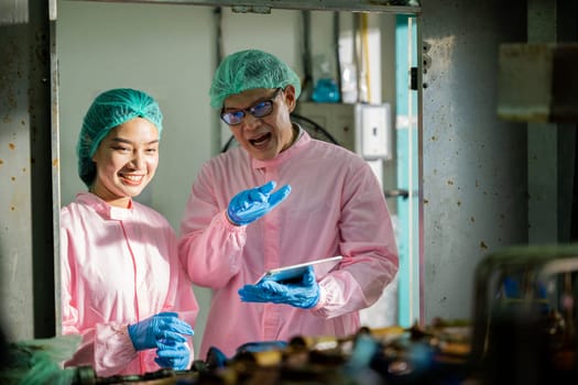 Two machine engineers at the beverages factory engage in quality control discussions using a digital tablet. They focus on examining manufacturing processes in the drinks production plant.