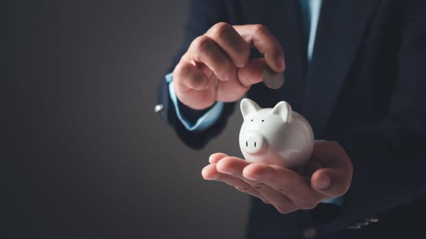 Businessman in suit is holding piggy bank. Finance Savings concept, Money saving and deposit for investment to get profit and dividend concept, Planning to income for savings and paying off expenses.
