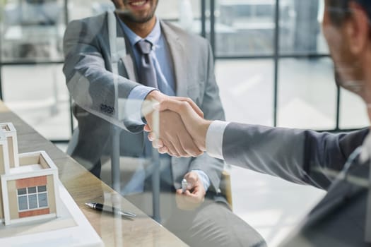 Businessmen shaking hands with house model on desk at table