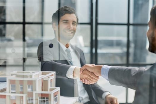 Businessmen shaking hands with house model on desk at table