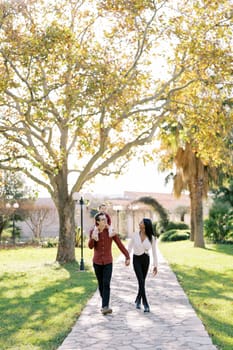 Dad with a little girl on his shoulders walks holding hands with mom in the park. High quality photo