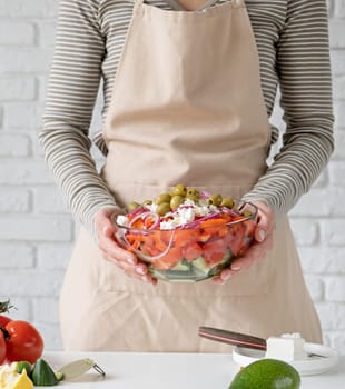 Cooking process of Greek Salad. Woman adding olives to bowl of Greek salad