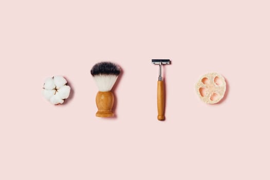 Natural bamboo sponge, shaver brush, razor and cotton flower on pink background. Flat lay, top view.