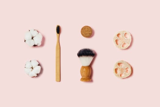 Bathroom accessories on pink background. Natural bamboo toothbrush, sponges, cotton flowers, shaving brush. Flat lay, top view.