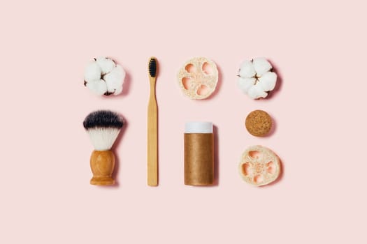 Natural bamboo toothbrush, paper tube, natural sponges, cotton flowers on pink background. Flat lay, top view.