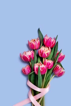 Greeting card with bouquet of tulips decorated with a pink ribbon on blue background, place for your text. Vertical picture.