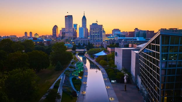 Sunset over Indianapolis: An aerial view of city skyline with diverse architecture, captured by a DJI Mavic 3 drone. The image highlights the serene canal reflecting the twilight hues and urban vibrancy of the city in 2023.