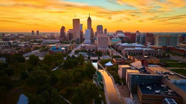 Golden hour illumination on Indianapolis city skyline with diverse skyscrapers, reflecting on a tranquil river, aerial shot, 2023