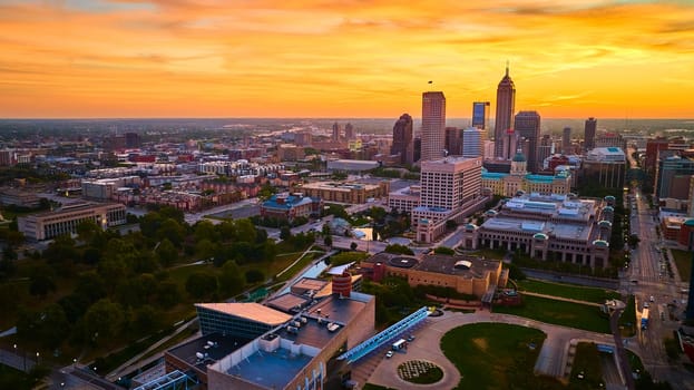 Golden Hour over Indianapolis - Aerial view showcasing the city's skyline with modern and historical architecture, green spaces and reflective waterways at sunset.