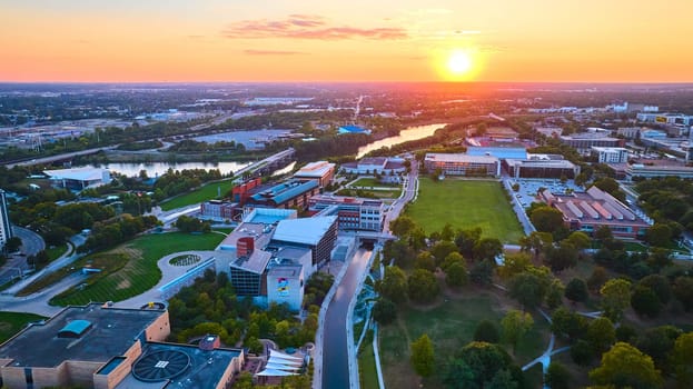 Sweeping aerial view of serpentine river through Indianapolis at sunset, showcasing an urban oasis with green spaces and modern architecture.