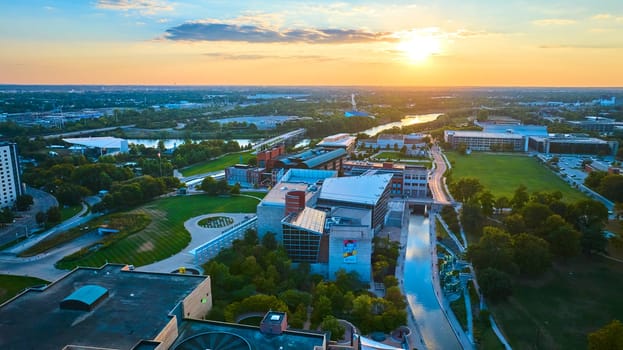 Golden hour cityscape of Indianapolis featuring a vibrant river, modern architecture, and an amphitheater captured in an aerial drone view