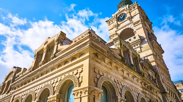 Sunny day view of Milwaukee's historic clock tower, captured from a unique low angle with a DJI Mavic 3 drone, showcasing stunning Gothic-Renaissance architecture against a picturesque blue sky.