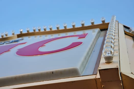 Close-up of vintage-style 'C' sign lined with clear light bulbs against a blue sky in Muncie, Indiana, reflecting retro Americana and optimism.