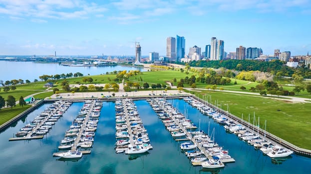 Aerial view of vibrant Milwaukee Marina with bustling sailboats, adjacent lush park, and urban skyline, representing harmony between city life and nature.