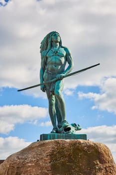 Bronze Statue of Native American holding spear on boulder in Muncie, Indiana, 2023, symbolizing cultural heritage and history