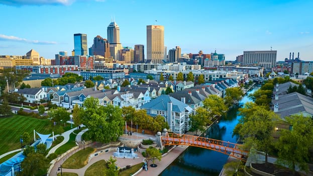 Aerial view of modern and historic skyline in Indianapolis during golden hour, showcasing a vibrant residential area with a canal and walking bridge