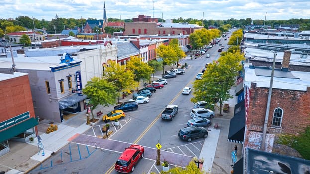 Elevated view of bustling small-town main street in Goshen, Indiana featuring vibrant architecture, active daily life, and early fall foliage, captured by DJI Mavic 3 drone in 2023.
