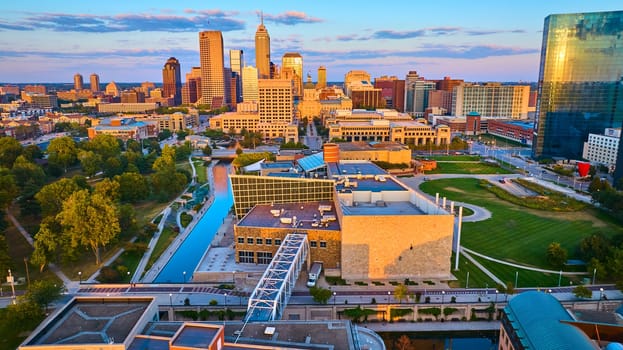 Golden hour aerial view of Indianapolis showcasing modern and traditional architecture, serene canal, and vibrant city park