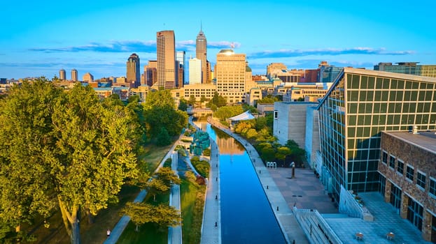 Golden Hour Glow Over Indianapolis - Aerial view of a serene urban canal cutting through vibrant cityscape with modern architecture and lush greenery, at sunset
