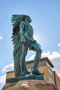 Majestic Native American warrior statue towers in Muncie, Indiana, accentuated by a modern urban backdrop - a testament to cultural heritage juxtaposed with contemporary architecture