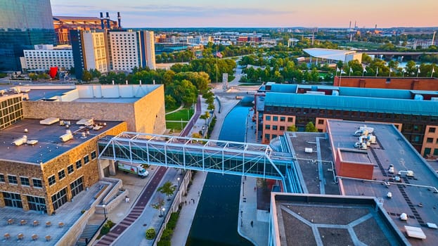 Sunrise over Indianapolis - Aerial view of a modern pedestrian bridge crossing a serene canal, surrounded by diverse architectural styles, at golden hour.