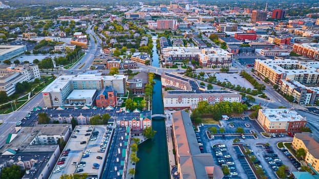 Aerial view of Indianapolis at golden hour, showcasing a tranquil canal, modern and traditional architecture, and bustling city life.
